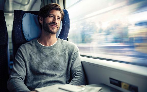 Ein Mann sitzt im Zug und schaut lächelnd aus dem Fenster.