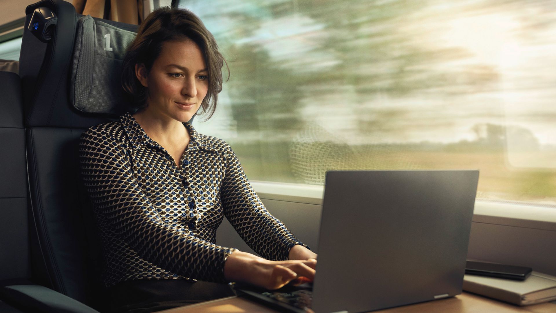 Frau sitzt im Zug und ist auf einen Laptop fokussiert.