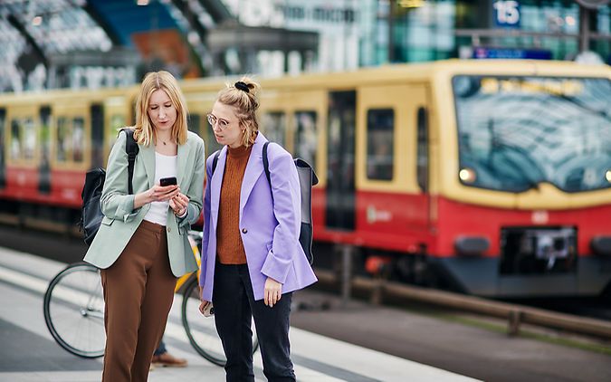 Junge Menschen schauen am Bahnsteig auf ein Handy