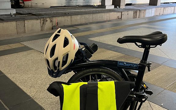 Klappfahrrad mit Helm und Rucksack auf Gleis, im Hintergrund ein ICE